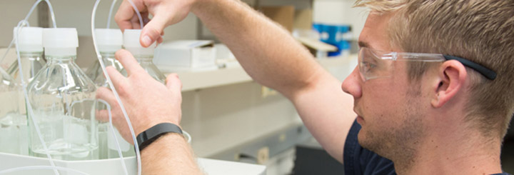 Man in safety glasses adjusts lab equipment.