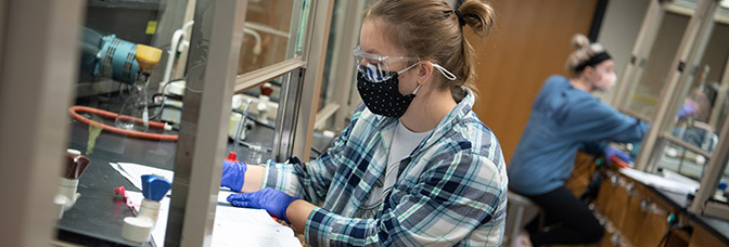 Person with a open book in a lab equipment behind plexi shield